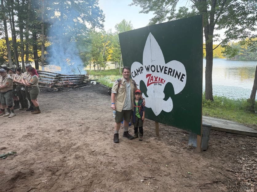 Scouts gathered with a leader at the camp gateway