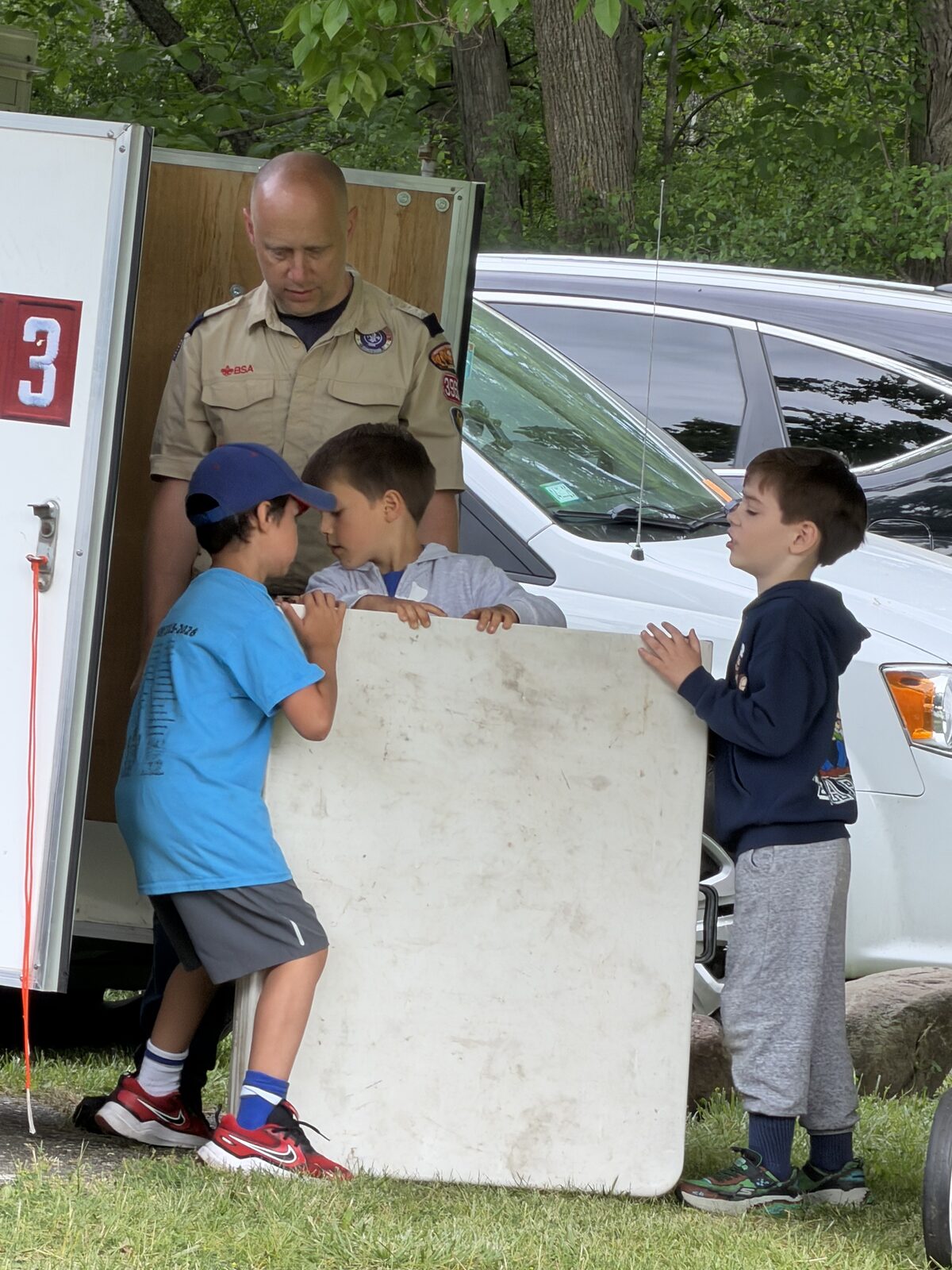Adult leader instructing Scouts beside the campsite trailer